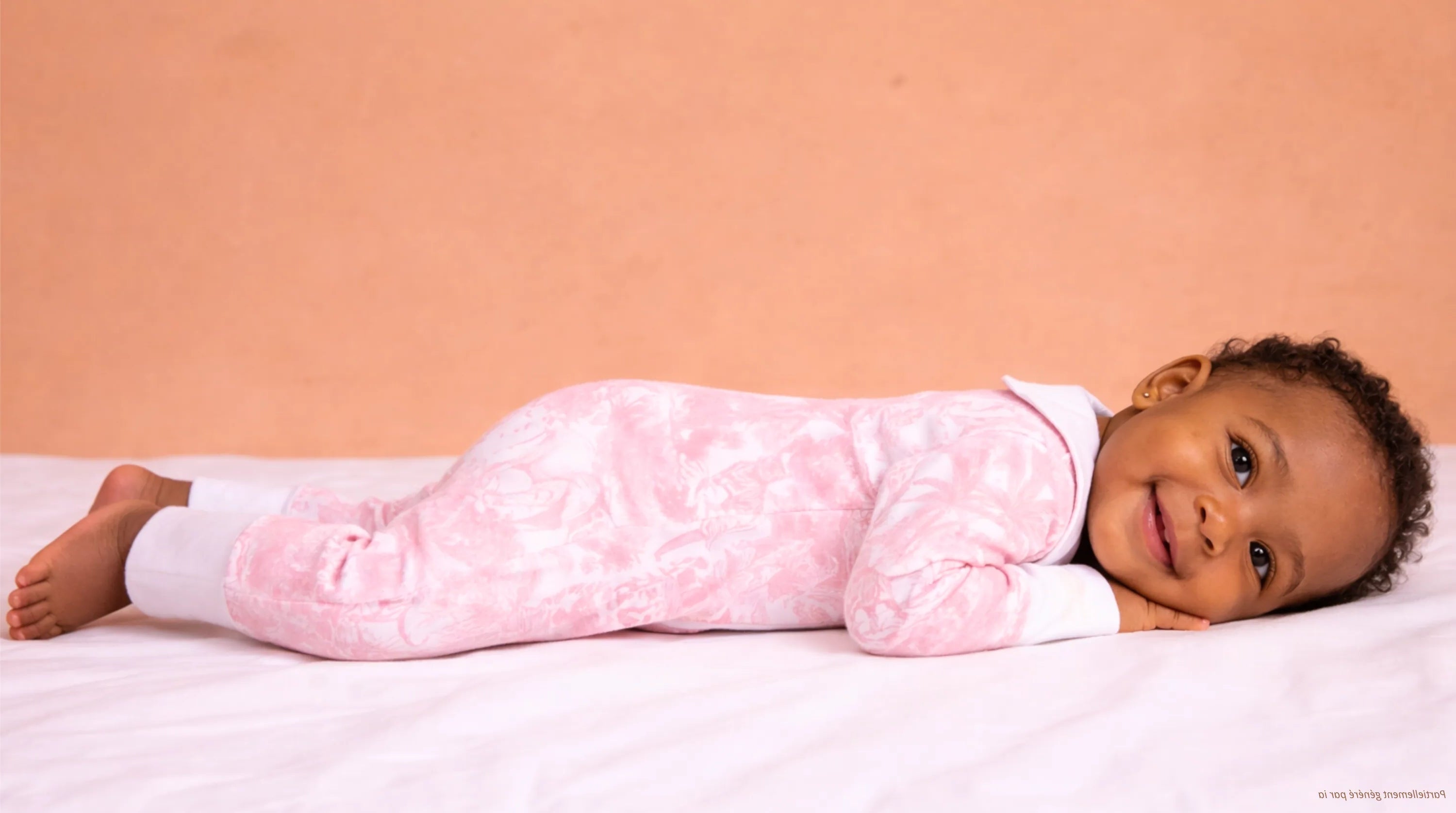 Bébé allongé sur le ventre, qui porte une combi-pyjama collection Rose Shayane.